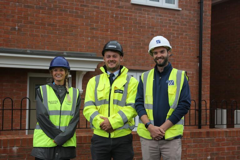 3 people standing in front of red brick house, they are making a high vis vest