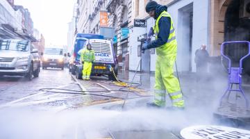 A photo of a street cleaner using a pressure washer to clean a pavement.