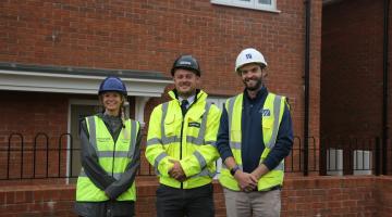 3 people standing in front of red brick house, they are making a high vis vest