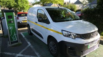 Electric small council van parked in car park next to an EV charger