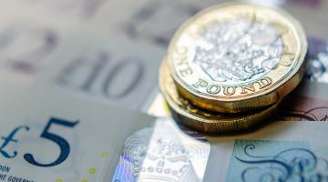 A photo of two pound coins resting on some pound notes.