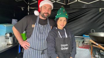 man in Christmas hat and woman in elf hat at market stall